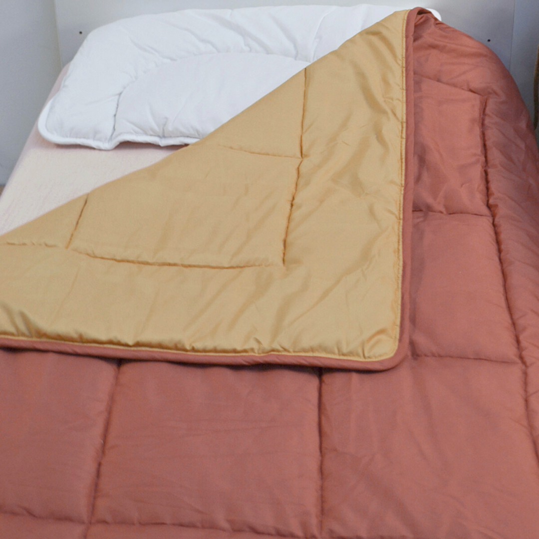 Ein ordentlich gemachtes Bett mit einem weißen Kissen und der Zelesta Kleinkinderbett - Sand & Terracotta Bettdecke, hellbraun auf der einen Seite und rostfarben auf der anderen - ideal für trockene Nächte mit seinem temperaturregulierenden, waschbaren Design.