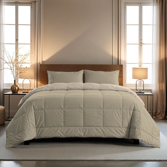 Ein ordentlich gemachtes Bett mit einer hellgrauen Bettdecke und Zelesta Comfort Duo Kissenbezug - Taupe 80x80cm, zwischen zwei Fenstern mit beigen Vorhängen und flankiert von passenden Nachttischen mit Lampen.