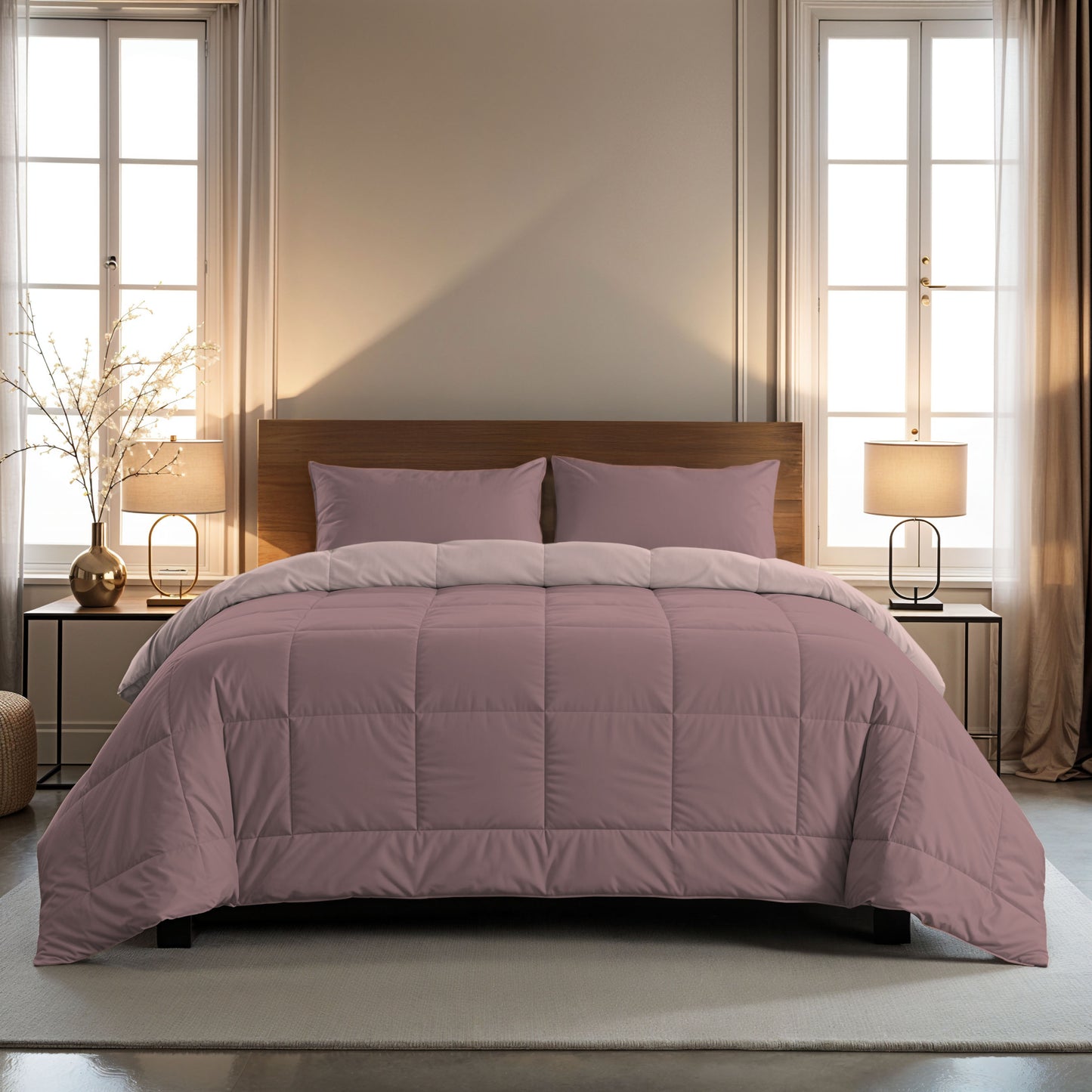 Ein ordentlich gemachtes Bett mit einer Zelesta Comfort Duo Bettdecke in Rosa & Hellrosa und passenden Kissen steht in der Mitte zwischen zwei Fenstern mit beigen Vorhängen, flankiert von Nachttischen mit Lampen.