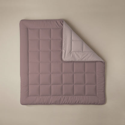 Eine Zelesta Comfort Duo Bettdecke in Rosa & Hellrosa mit einem gesteppten Gittermuster liegt flach auf einer beigen Fläche, eine Ecke ist umgedreht, um die hellere Unterseite zu zeigen.