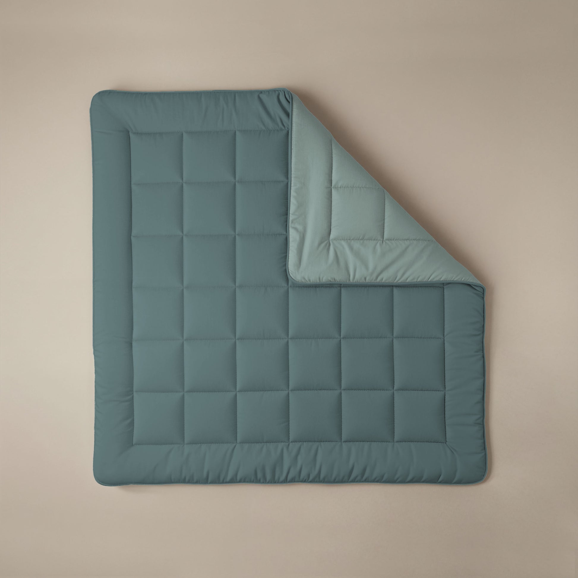 Eine Zelesta Comfort Duo Bettdecke in Mineral & Hellblau mit quadratischen Nähten liegt flach auf einer beigen Fläche, eine Ecke ist zurückgeklappt, um das hellere Innenfutter zu zeigen.