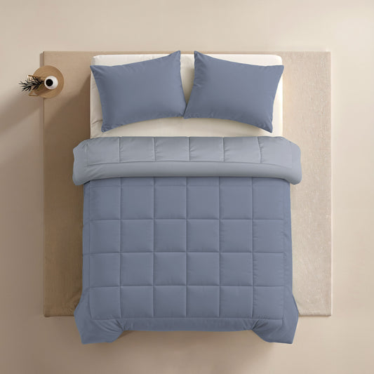 Ein ordentlich gemachtes Bett mit einer blauen Bettdecke und passendem Zelesta Comfort Duo Kissenbezug - Arktisch (80x80cm), fotografiert von oben auf einem beigen Teppich.