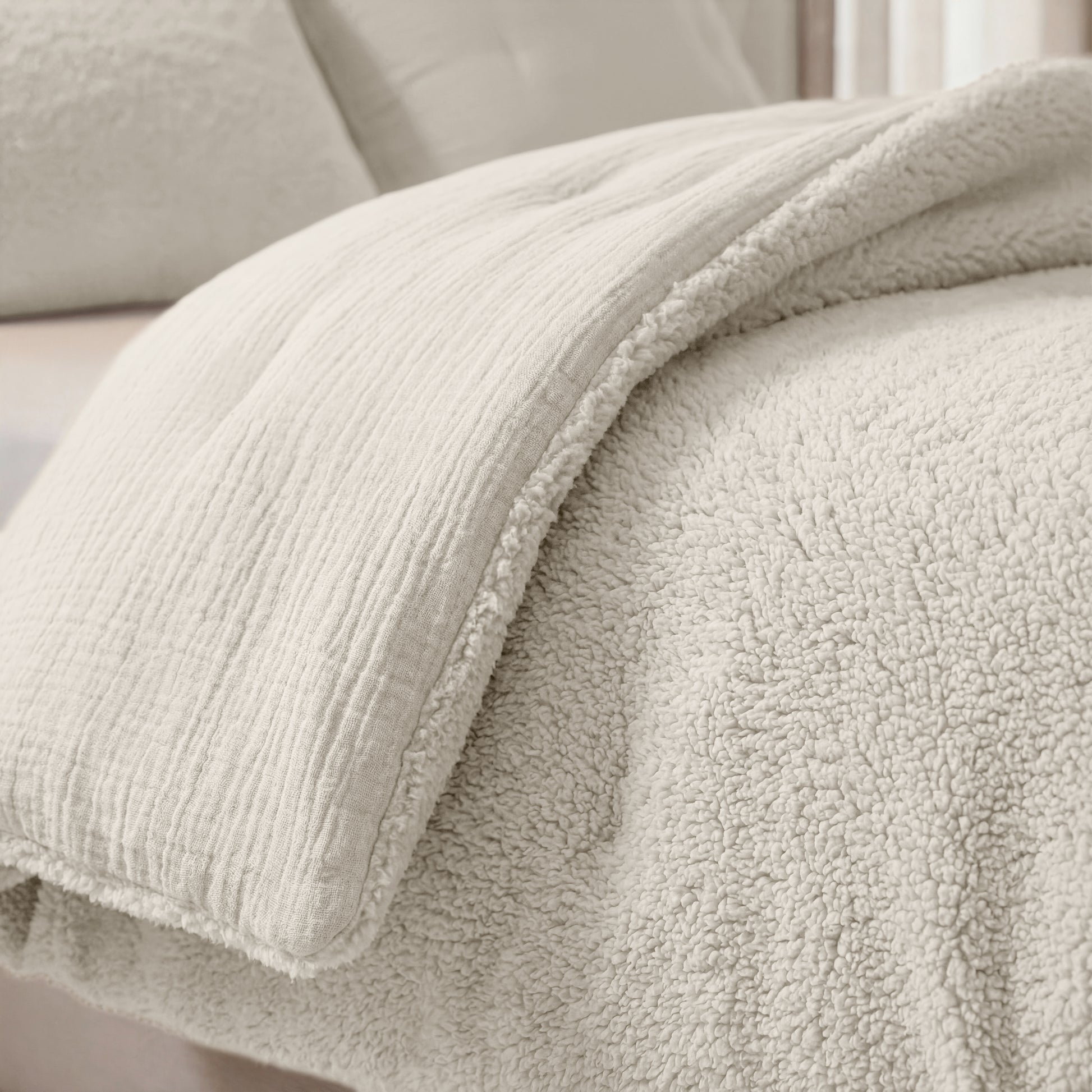 Eine Nahaufnahme eines ordentlich gemachten Bettes mit der Zelesta Teddy Baumwolle Musselin - Beige, einer weichen, flauschigen Steppdecke in hellen Beigetönen.