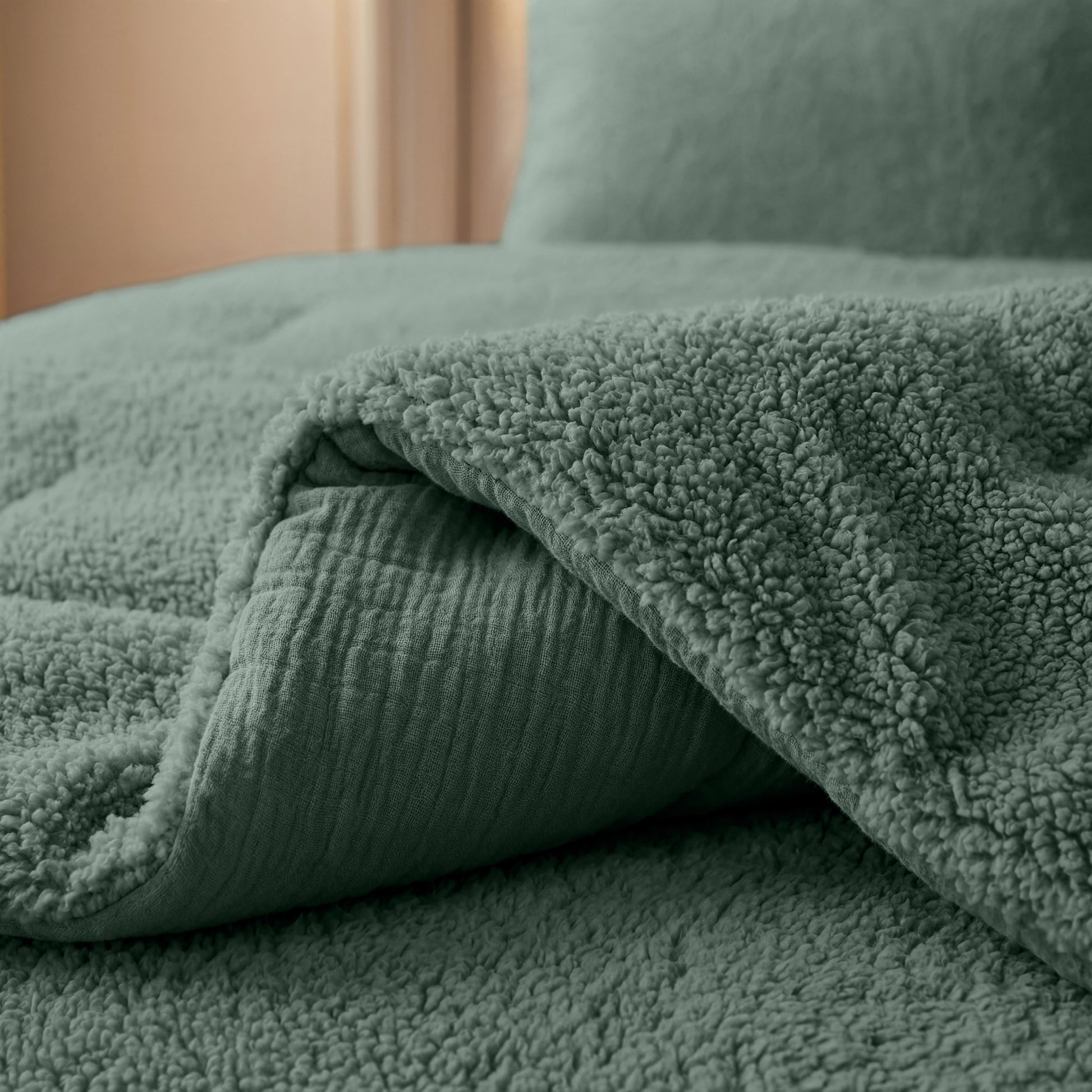 Eine Nahaufnahme der Zelesta Teddy Baumwolle Musselin - Grün, strukturiert und über eine passende grüne Tagesdecke drapiert, mit einem Kissen im Hintergrund.