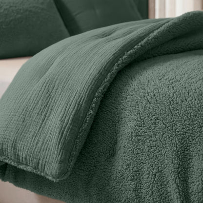 Nahaufnahme eines Bettes mit grüner Strukturdecke und passender flauschiger Sherpa-Decke, die mit dem Zelesta Teddy Baumwolle Musselin - Grün für zusätzliche Wärme und Komfort sorgt.