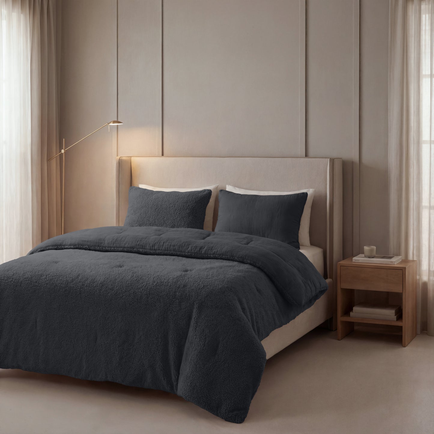 Ein ordentlich gemachtes Bett mit einem beige gepolsterten Kopfteil, dunkelgrauer Bettwäsche, zwei Kissen und dem Zelesta Teddy Baumwolle Musselin - Anthrazit. Nachttisch aus Holz und raumhohe Fenster mit hellen Vorhängen.