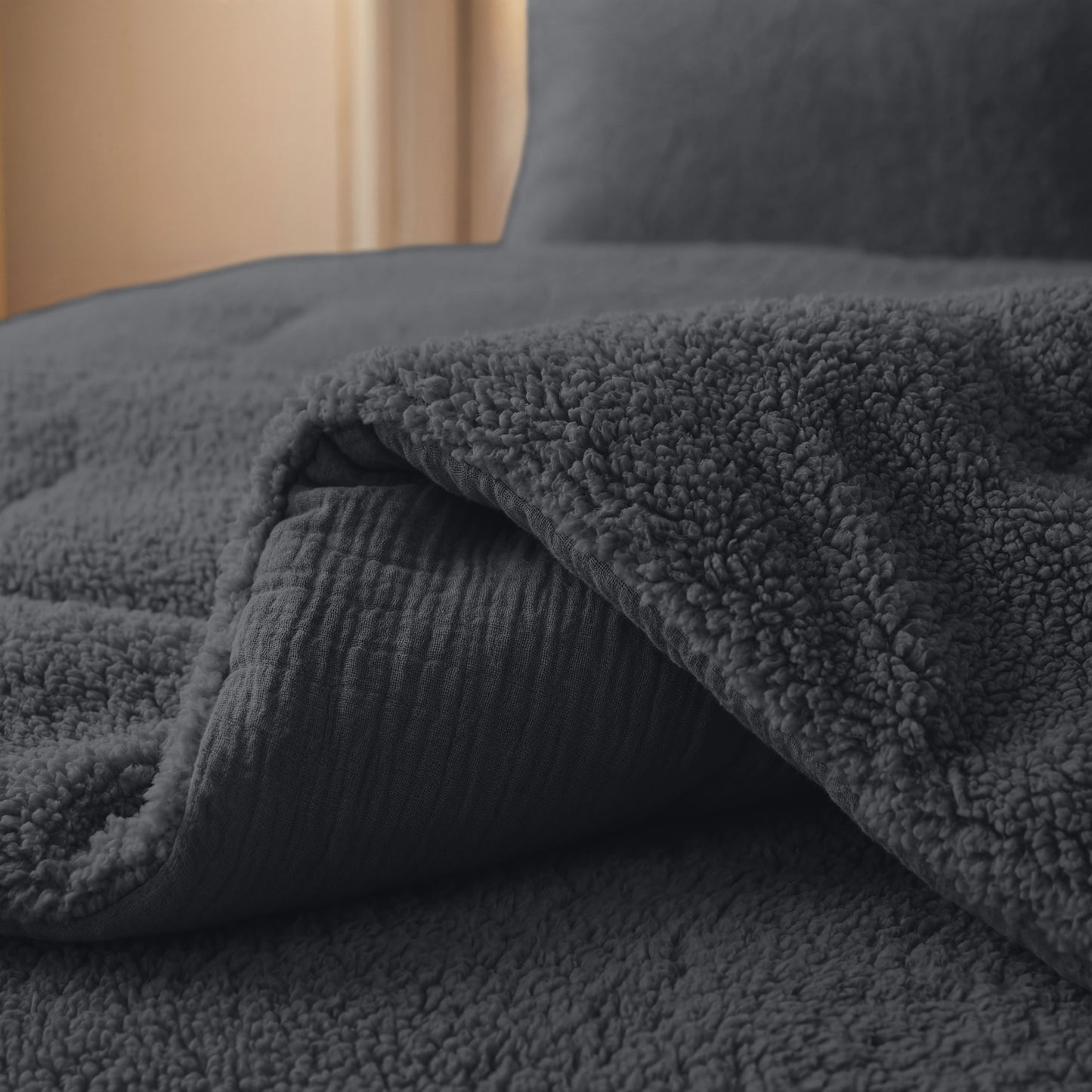 Die Nahaufnahme eines ordentlich gemachten Bettes zeigt die Zelesta Teddy Baumwolle Musselin - Anthrazit, eine dunkelgraue, strukturierte Decke aus atmungsaktiver Baumwolle, die für zusätzlichen Komfort teilweise zurückgefaltet ist.