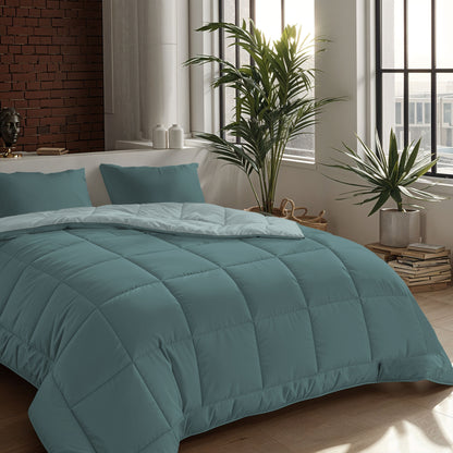 Ein ordentlich gemachtes Bett mit einer Zelesta Comfort Duo Bettdecke in Mineral & Hellblau und zwei Kissen in einem modernen Schlafzimmer mit großen Fenstern, Topfpflanzen und einem Stapel Bücher auf dem Boden.