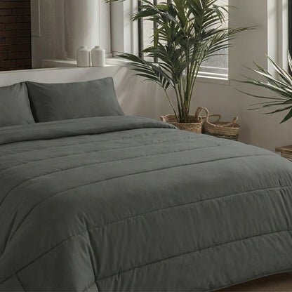 Ein ordentlich gemachtes Bett mit dunkelgrauer Mikrofaser-Bettwäsche und Zelesta Comfort Uni Kissenbezügen Set von 2 - Anthrazit (80x80cm) steht neben großen Fenstern und zwei Topfpflanzen in einem modernen, minimalistischen Schlafzimmer.