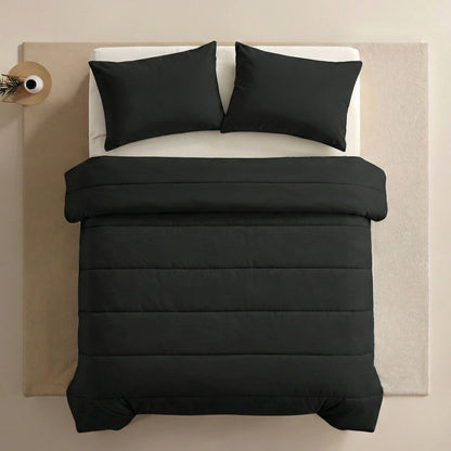 Ein ordentlich gemachtes Bett mit einer schwarzen Bettdecke und zwei Zelesta Comfort Uni Kissenbezügen Set von 2 - Schwarz (80x80cm), platziert auf einem hellen Teppich neben einem kleinen runden Beistelltisch mit einer Vase.