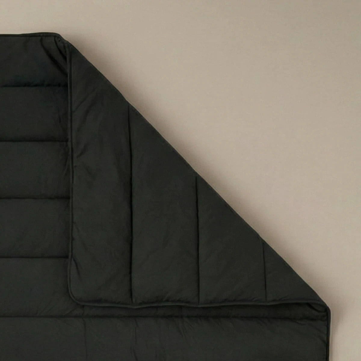 Eine sauber gefaltete Ecke der Zelesta Comfort Uni Bettdecke - Schwarz wird vor einem schlichten, hellen Hintergrund gezeigt.