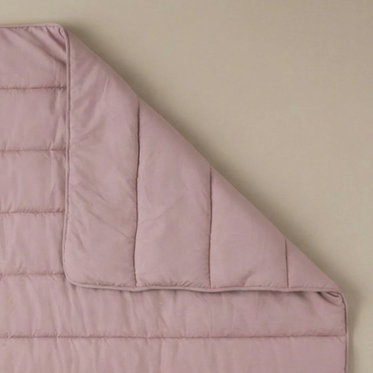 Eine Zelesta Comfort Uni Bettdecke in Altrosa liegt flach auf einer beigen Unterlage, wobei eine Ecke gefaltet ist, um das kuschelige und stilvolle Steppdesign zu enthüllen.