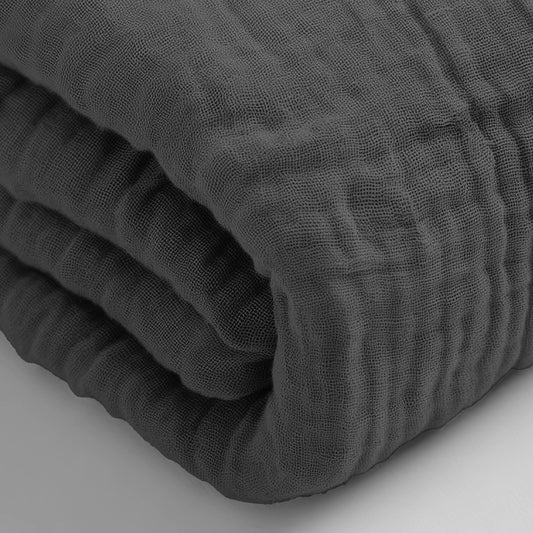 Eine Nahaufnahme des anthrazitfarbenen Musselin-Spannbettlakens, gefaltet, um sein strukturiertes Gewebe zu zeigen, auf einer hellen Fläche.
