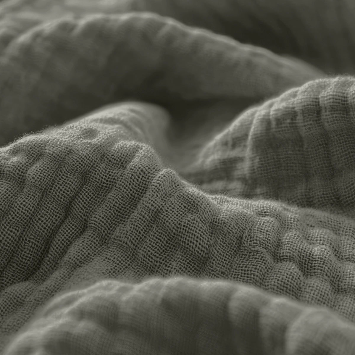 Nahaufnahme des texturierten, faltigen Musselin Spannbettlaken - Grey-Green, das seine sichtbaren Webmuster und weichen Falten in einer gedeckten Farbpalette zeigt.