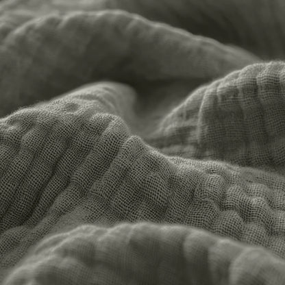 Nahaufnahme des texturierten, faltigen Musselin Spannbettlaken - Grey-Green, das seine sichtbaren Webmuster und weichen Falten in einer gedeckten Farbpalette zeigt.