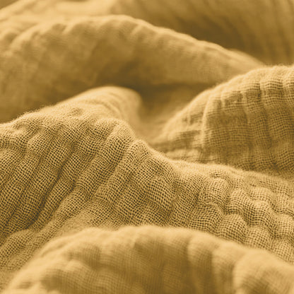 Nahaufnahme des strukturierten, faltigen Musselin-Spannbettlakens in Ockergelb, das seine gewebte Struktur und die weichen Falten betont.