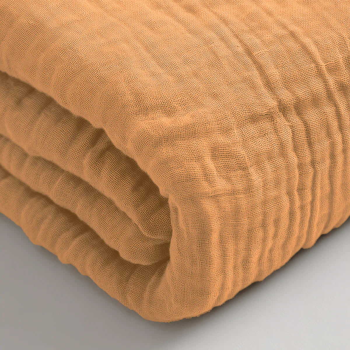 Eine Nahaufnahme eines gefalteten, strukturierten Musselin Spannbettlaken - Taupe, das auf einer flachen Oberfläche liegt.