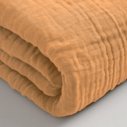 Eine Nahaufnahme eines gefalteten, strukturierten Musselin Spannbettlaken - Taupe, das auf einer flachen Oberfläche liegt.