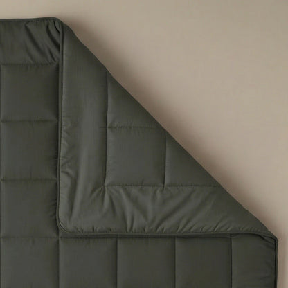 Die Zelesta Pure Uni Bettdecke - Olivschwarz ist auf einer beigen Oberfläche ausgebreitet, wobei eine umgeschlagene Ecke ihre Nähte und ihre Dicke zur Geltung bringt - ideal für atmungsaktiven Schlafkomfort.