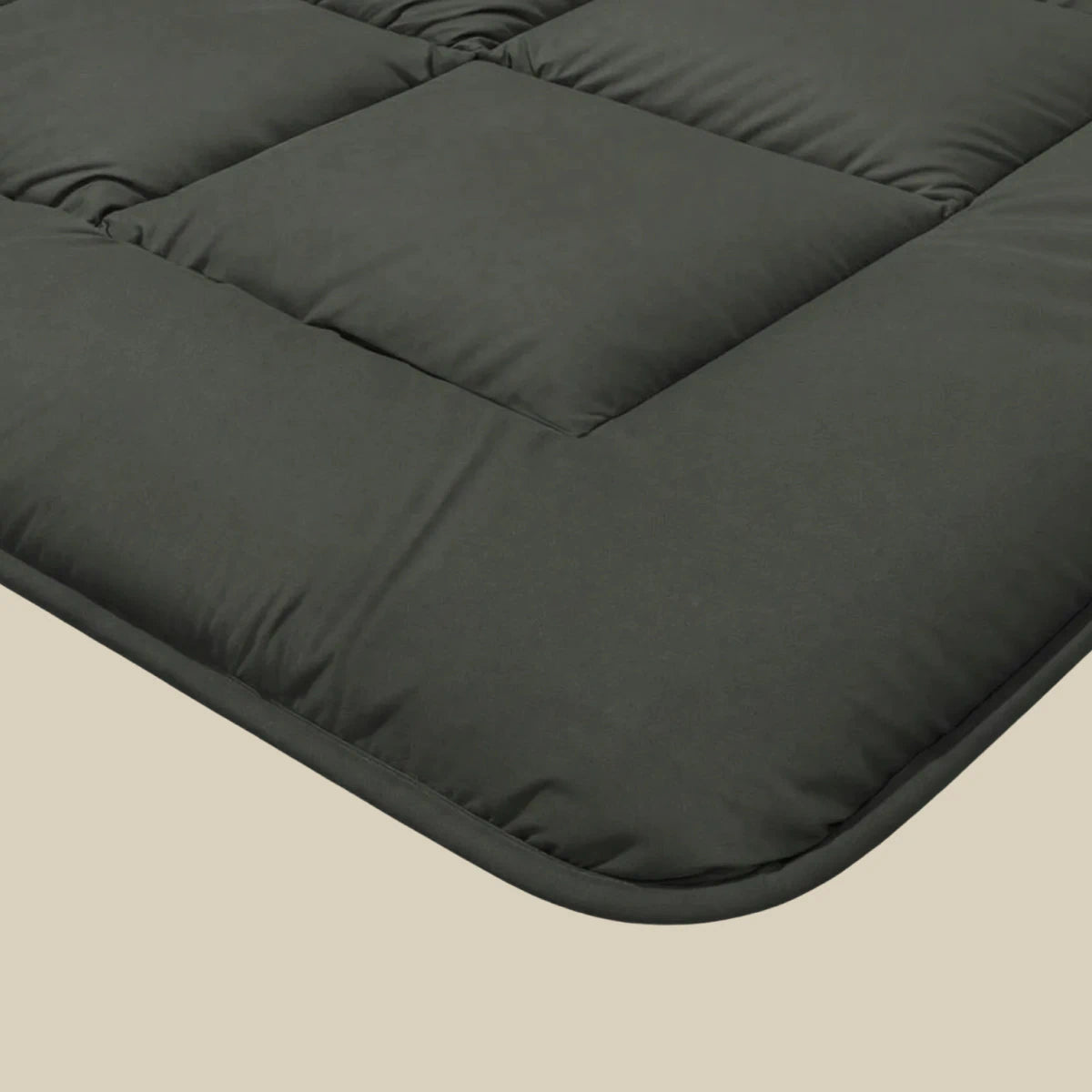Nahaufnahme der Zelesta Pure Uni Bettdecke in olivschwarz, mit weicher, gesteppter Struktur für optimalen Schlafkomfort, vor einem beigen Hintergrund.