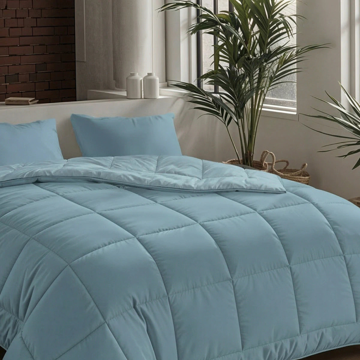 Ein ordentlich gemachtes Bett mit der Zelesta Pure Uni Bettdecke in Sereneblau und Kissen, in einem hellen Raum mit großen Fenstern, Grünpflanzen und dekorativen Gläsern auf der Fensterbank für atmungsaktiven Schlafkomfort.