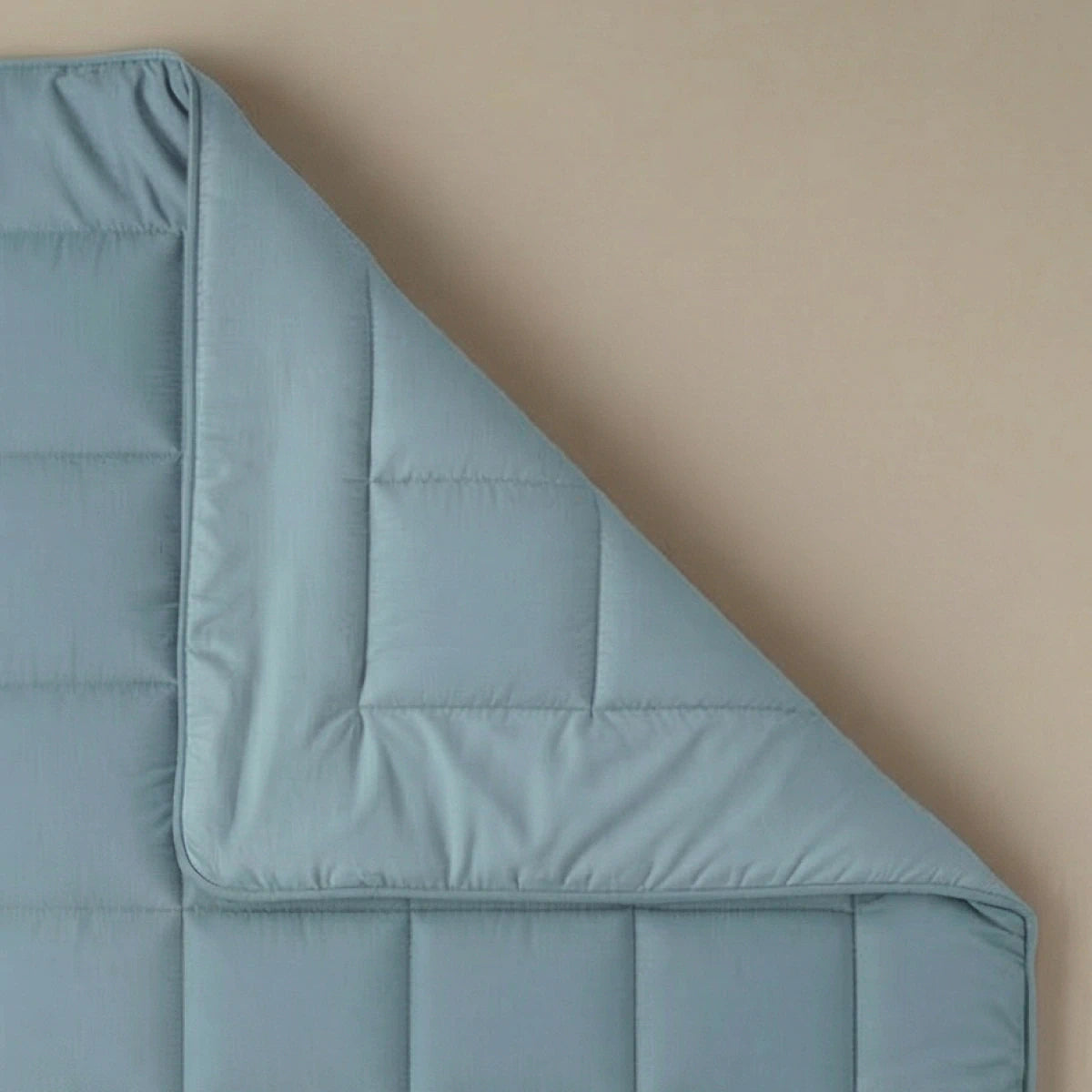 Die Zelesta Pure Uni Bettdecke - Sereneblau, eine hellblaue Baumwollbettdecke mit umgeschlagener Ecke, präsentiert sich auf einer beigen Oberfläche und bietet atmungsaktiven Schlafkomfort für alle, die Wert auf nachhaltige Bettdecken legen.