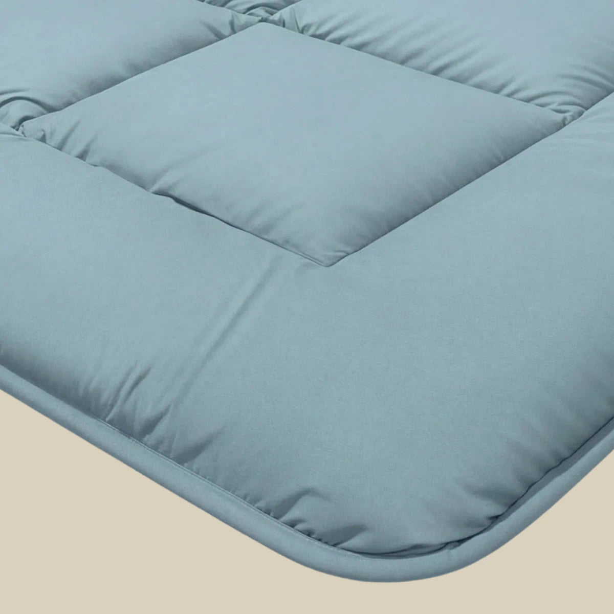 Nahaufnahme der Zelesta Pure Uni Bettdecke in Sereneblau: hellblauer, gepolsterter Bezug mit quadratischen Nähten und glatter Stoffoberfläche, der einen angenehmen Schlafkomfort für eine erholsame Nachtruhe bietet.