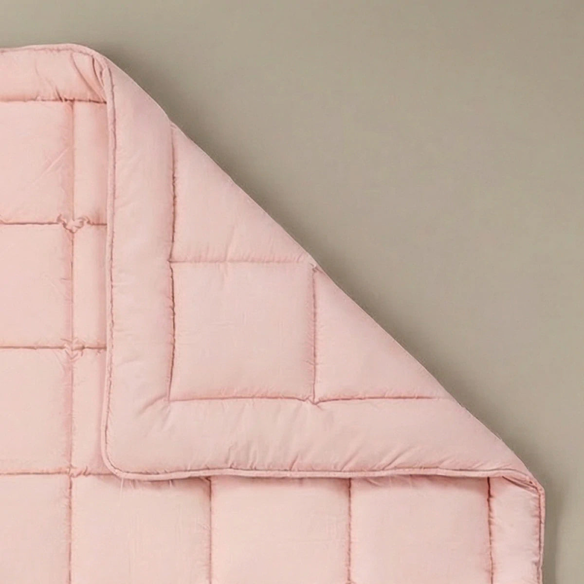 Die Zelesta Pure Uni Bettdecke in Zartrosa mit ihrer quadratischen Naht ist an einer Ecke gefaltet auf einem beigen Hintergrund zu sehen - eine elegante, nachhaltige Ergänzung Ihrer Dekbedden-Kollektion.