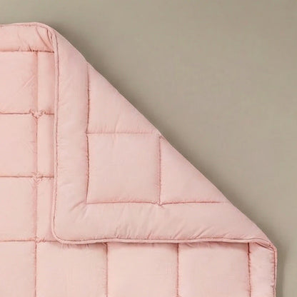 Die Zelesta Pure Uni Bettdecke in Zartrosa mit ihrer quadratischen Naht ist an einer Ecke gefaltet auf einem beigen Hintergrund zu sehen - eine elegante, nachhaltige Ergänzung Ihrer Dekbedden-Kollektion.