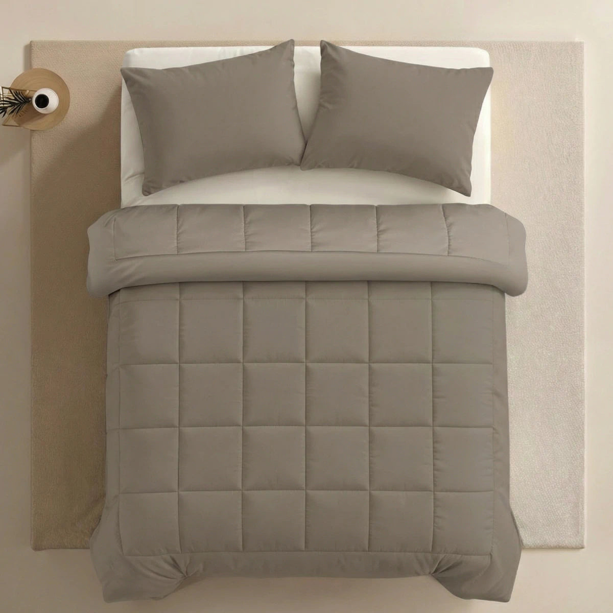 Ein ordentlich gemachtes Bett mit der Zelesta Pure Uni Bettdecke in Anthrazitgrau, zwei passenden Kissen, einem weißen Spannbetttuch auf einem hellen Teppich für dauerhaften Komfort und einem kleinen runden Nachttisch an der Seite.