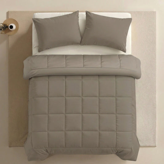 Ein ordentlich gemachtes Bett mit der Zelesta Pure Uni Bettdecke in Anthrazitgrau, zwei passenden Kissen, einem weißen Spannbetttuch auf einem hellen Teppich für dauerhaften Komfort und einem kleinen runden Nachttisch an der Seite.