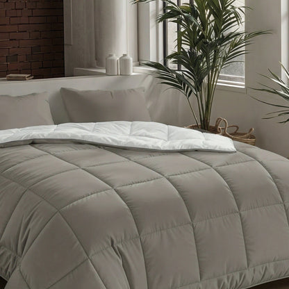 Ein ordentlich gemachtes Bett mit der Zelesta Pure Uni Bettdecke in Anthrazitgrau, weißen Laken und grauen Kissen neben einem Fenster mit Topfpflanzen und zwei weißen Deko-Gläsern auf der Fensterbank.