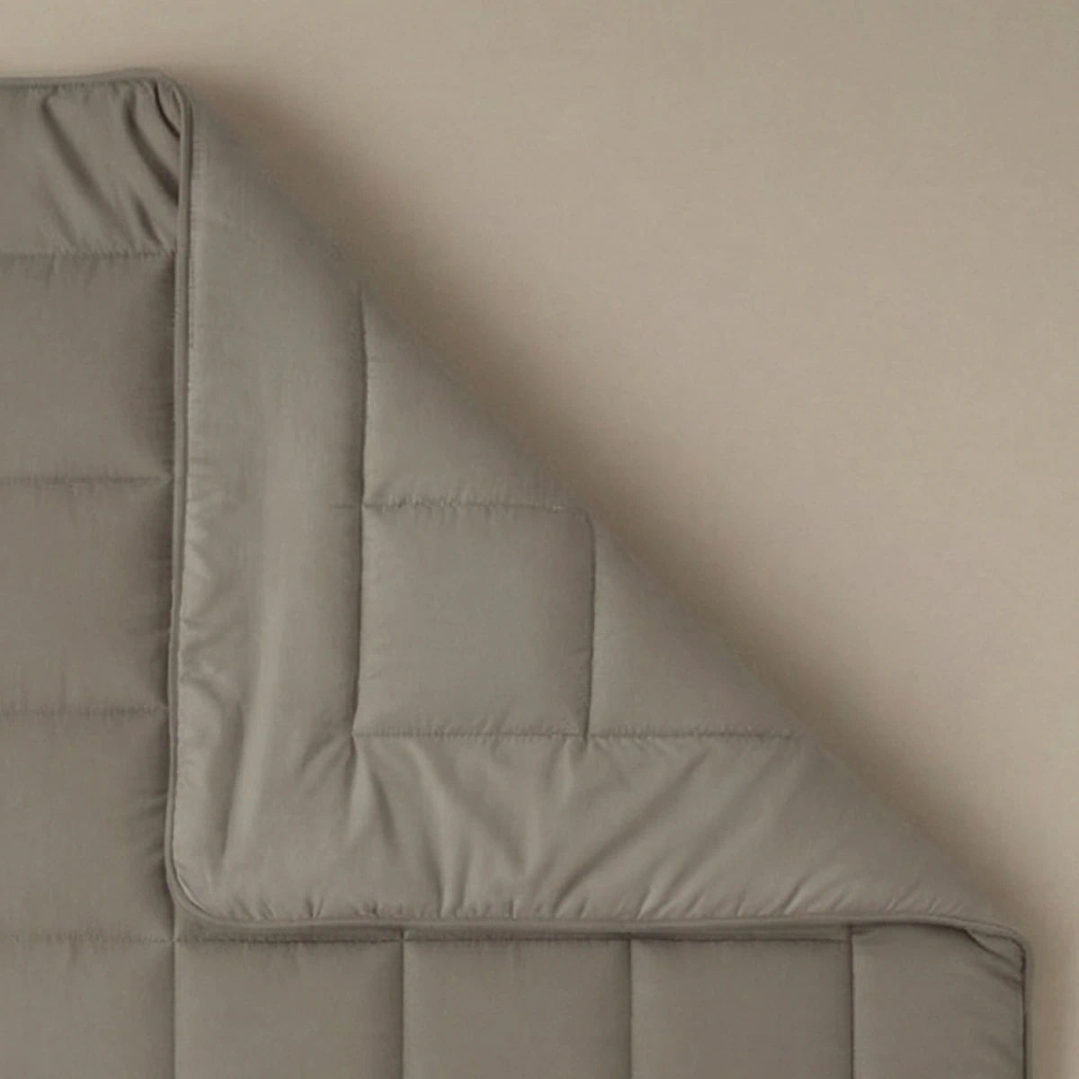 Eine sauber gefaltete Ecke der Zelesta Pure Uni Bettdecke in Anthrazitgrau ruht auf einer beigen Oberfläche.