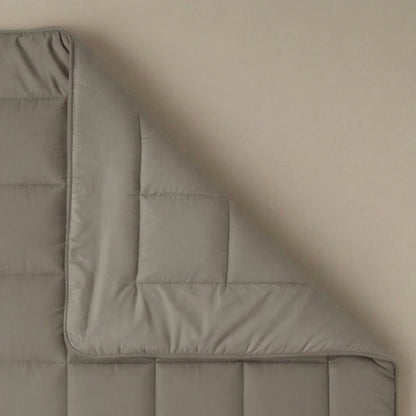Eine sauber gefaltete Ecke der Zelesta Pure Uni Bettdecke in Anthrazitgrau ruht auf einer beigen Oberfläche.